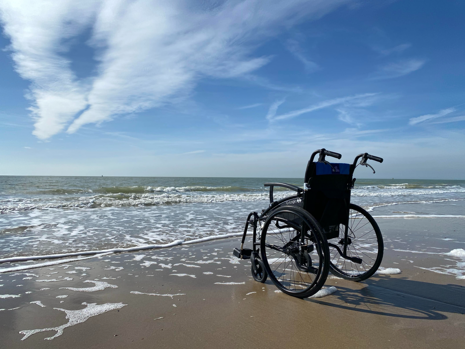 Wheelchair on a sandy beach with ocean waves and blue sky.